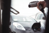 Hand of man holding car charger at electric vehicle charging station — Stock Photo