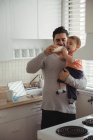 Отец кормит мальчика молочной бутылкой на кухне — стоковое фото