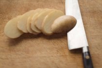 Close-up de batatas fatiadas e faca na tábua de corte — Fotografia de Stock