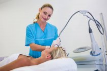Mujer que recibe tratamiento de depilación láser en la frente en el salón de belleza - foto de stock