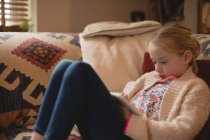 Menina sentada no sofá e usando tablet digital na sala de estar em casa — Fotografia de Stock