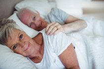 Улыбающаяся пожилая пара лежит на кровати в спальне — стоковое фото