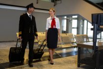 Pilota e hostess che camminano con le borse dei carrelli nel terminal dell'aeroporto — Foto stock