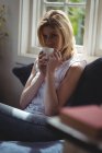 Mulher bonita tomando café na sala de estar em casa — Fotografia de Stock