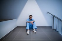 Напружена медсестра чоловічої статі сидить в коридорі лікарні — стокове фото