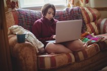 Женщина сидит на диване и пользуется ноутбуком в гостиной дома — стоковое фото