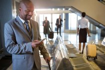 Бизнесмен, использующий мобильный телефон в зоне ожидания в терминале аэропорта — стоковое фото