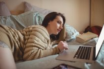 Bella donna sdraiata e utilizzando il computer portatile sul letto a casa — Foto stock