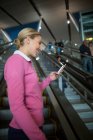 Navetteur féminin utilisant un téléphone mobile sur l'escalator à l'aéroport — Photo de stock