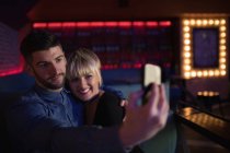 Улыбающаяся пара делает селфи на мобильном телефоне в баре — стоковое фото