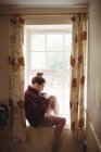 Frau sitzt auf Fensterbank und trinkt Kaffee zu Hause — Stockfoto