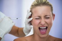 Nahaufnahme einer verängstigten Frau, die schreit, während sie eine Injektion aus kosmetischer Behandlung erhält — Stockfoto