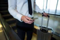 Средняя секция бизнесмена на эскалаторе с помощью мобильного телефона в аэропорту — стоковое фото