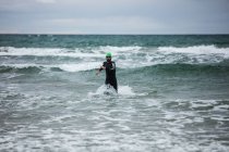 Atleta en traje de neopreno corriendo en el mar - foto de stock