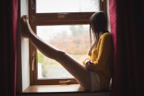 Frau sitzt auf Fensterbank und schaut zu Hause durch — Stockfoto