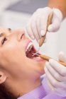 Primer plano del dentista que examina los dientes de las mujeres con herramientas - foto de stock