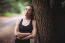 Thoughtful woman leaning on tree in forest — Stock Photo