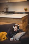Donna sdraiata sul divano mentre ascolta musica con il cellulare a casa — Foto stock