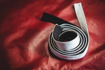 Rolled karate white and black belt on red background — Stock Photo