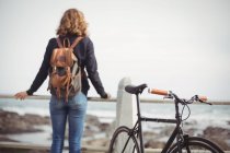 Visão traseira de uma mulher de pé com a bicicleta perto da praia — Fotografia de Stock