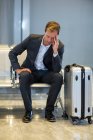 Напряженный бизнесмен сидит в зале ожидания с багажом в терминале аэропорта — стоковое фото