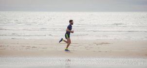 Atleta bonito correndo ao longo da praia — Fotografia de Stock