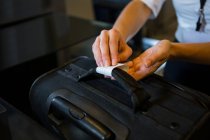 Персонал женского пола прикрепляет этикетку регистрации к багажу в терминале аэропорта — стоковое фото