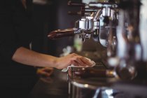 Sección media de la camarera limpiando la máquina de café espresso con servilleta en la cafetería - foto de stock