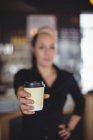 Portrait of waitress standing with disposable coffee cup in cafe — Stock Photo