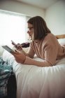 Woman lying on bed using mobile phone and digital tablet in bedroom — Stock Photo