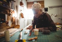 Aufmerksame Handwerkerin schneidet in Werkstatt ein Stück Leder — Stockfoto