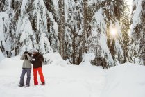 Couple with address card looking through binoculars on snowy landscape — Stock Photo