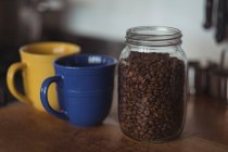 Primer plano de un frasco de granos de café tostados y tazas de café - foto de stock
