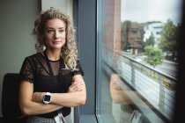 Thoughtful businesswoman standing with arms crossed in office — Stock Photo