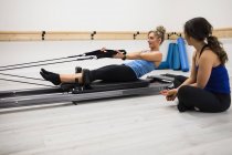 Female trainer assisting woman with stretching exercise on reformer in gym — Stock Photo