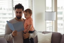 Padre leggendo libro mentre tiene il suo bambino a casa — Foto stock
