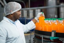 Arbeiter kontrolliert Orangensaftflaschen in Fabrik — Stockfoto