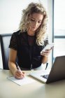 Geschäftsfrau schreibt im Büro mit Handy auf Notizblock — Stockfoto