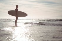 Силует вдумливі серфер, стоячи з дошки для серфінгу на пляжі — стокове фото