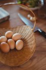 Eier im Weidenkorb auf Holztisch in der Küche — Stockfoto
