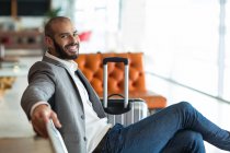 Retrato de un hombre de negocios sonriente sentado en una silla en la sala de espera en la terminal del aeropuerto - foto de stock
