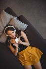 Frau liegt auf Sofa, während sie zu Hause mit Handy Musik hört — Stockfoto