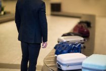 Mid-section of businessman waiting for luggage in baggage claim area at airport — Stock Photo