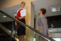 Personnel féminin interagissant avec un homme d'affaires sur un escalier roulant à l'aéroport — Photo de stock