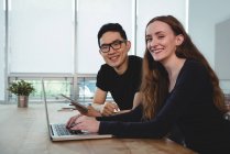 Портрет улыбающихся бизнес-руководителей с цифровым планшетом и ноутбуком, сидящих в офисе — стоковое фото