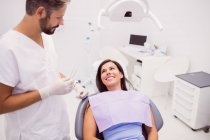 Dentista hablando con una paciente sonriente acostada en una silla en la clínica - foto de stock