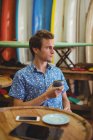 Мужчина, сидящий в магазине серфинга с чашкой кофе — стоковое фото