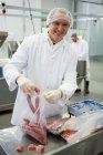 Porträt eines männlichen Metzgers, der in einer Fleischfabrik Rohwürste verpackt — Stockfoto