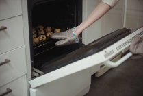 Brazo de mujer horneando galletas en horno doméstico - foto de stock