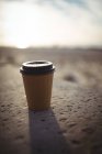 Nahaufnahme einer braunen Einweg-Kaffeetasse auf Sand — Stockfoto
